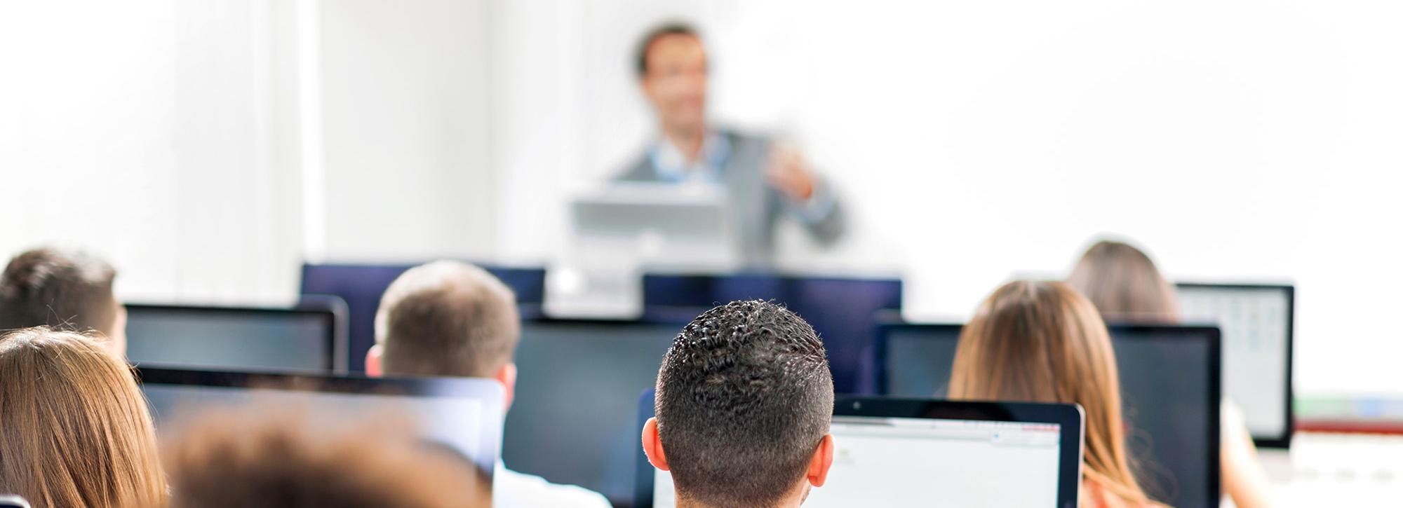 Picture of people seating at a computer listening to a professional giving them a training course