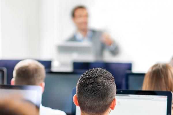 Picture of people seating at a computer listening to a professional giving them a training course